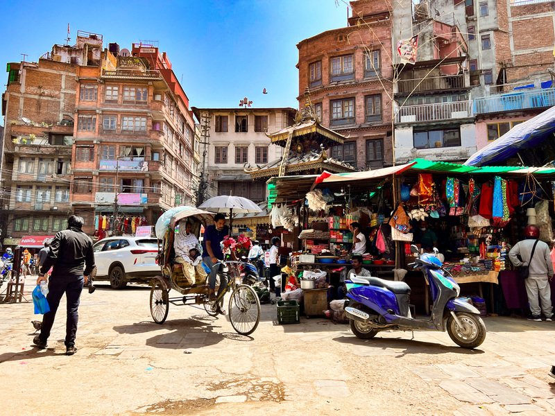 StraĂźenszene mit Rikscha und Marktstand in Kathmandu