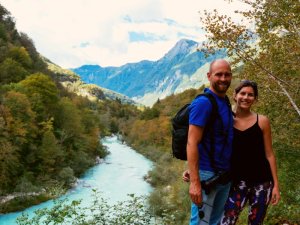 Lächelnder Mann und Frau auf einem Hügel mit Blick auf einen leuchtend türkisfarbenen Fluss in einem grünen Tal mit Bergen im Hintergrund im Soča-Tal Slowenien