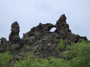 Vulkanische Felsformationen mit natürlicher Öffnung in der rauen Landschaft Islands unter bewölktem Himmel