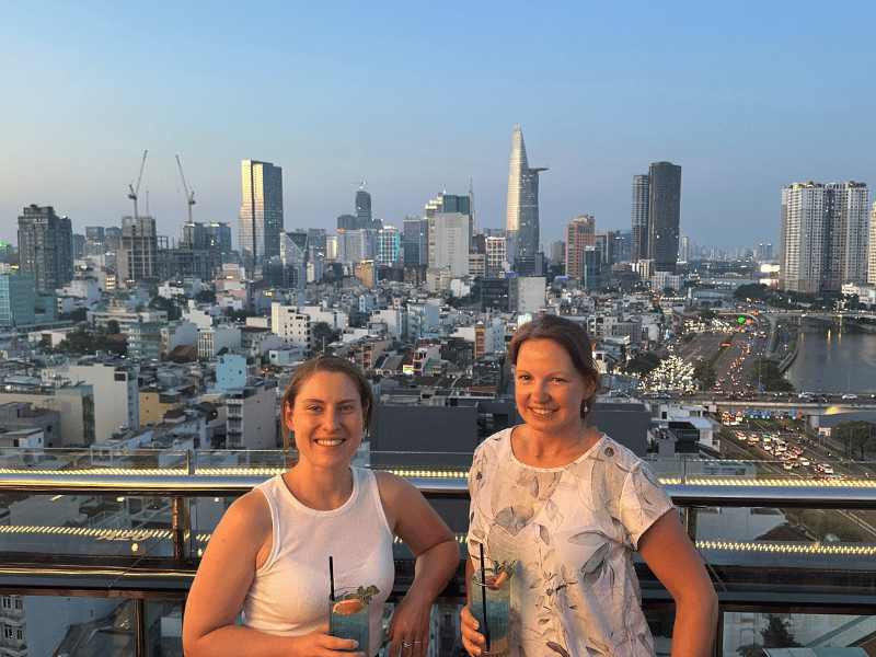 Zwei Reisende mit einem Cocktail in einer Rooftop Bar mit Blick auf Ho-Chi-Minh-Stadt in Vietnam