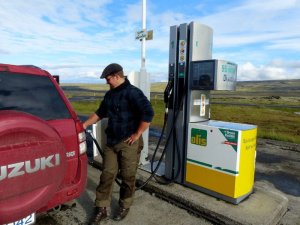 Mann mit Kappe tankt einen roten Suzuki SUV an einer Olís-Tankstelle in Island