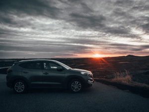 Dunkelgrauer SUV steht bei Sonnenuntergang unter bewölktem Himmel an einer Straße in Island
