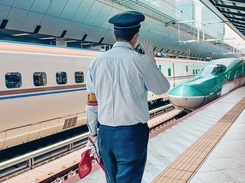 Schaffner im Bahnhof in Tokio bei der Einfahrt eines Shinkansen