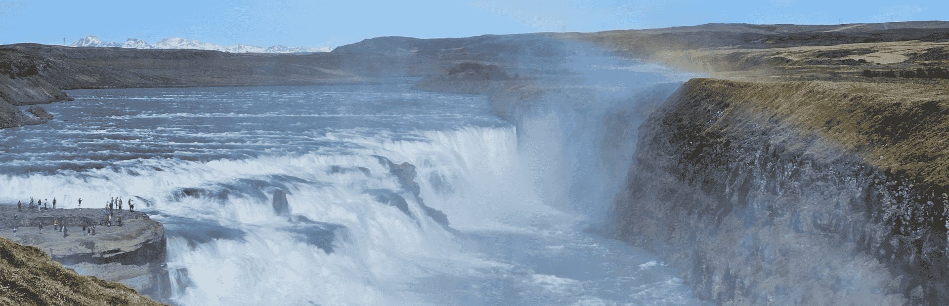 Touristen stehen am imposanten Gullfoss-Wasserfall in der rauen Landschaft Islands mit aufsteigendem Sprühnebel und schneebedeckten Bergen im Hintergrund