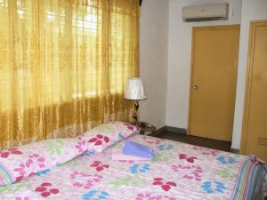 Schlafzimmer mit Blumenbettdecke, goldenen Vorhängen, Nachttischlampe und Klimaanlage über einer Holztür in Baracoa, Kuba
