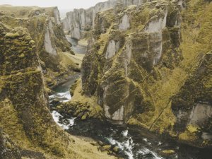 Fluss fließt durch eine tiefe Schlucht mit steilen moosbedeckten Wänden in Island