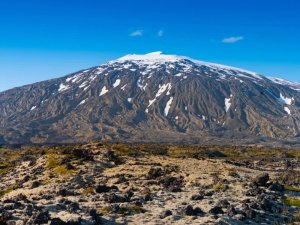 Schneebedeckter Vulkan über einer rauen Lavalandschaft in Island unter klarem blauem Himmel
